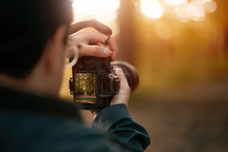 Photo for Isolated Close-up of a man holding a modern photo camera while looking at the screen. Horizontal banner image of camera using with the screen visible. Concept of an amateur taking photos in the forest - Royalty Free Image
