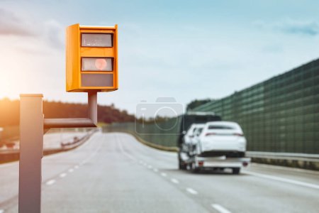 Una cámara de velocidad equipada con radar monitorea el tráfico en una carretera, parpadea una luz amarilla cuando atrapa un automóvil que excede el límite de velocidad y utiliza tecnología para identificar el vehículo y hacer cumplir la ley..