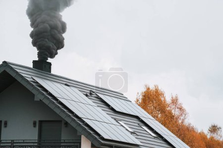 Photo for Dark smoke comes out of the chimney of a modern house during the late autumn and winter. Heating with solid fuel. The concept of environmental pollution - Royalty Free Image