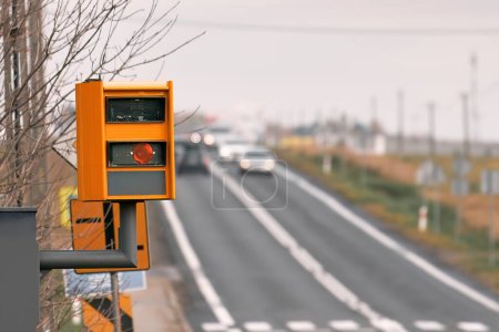 Foto de Una cámara de velocidad equipada con radar monitorea el tráfico en una carretera, parpadea una luz amarilla cuando atrapa un automóvil que excede el límite de velocidad y utiliza tecnología para identificar el vehículo y hacer cumplir la ley.. - Imagen libre de derechos