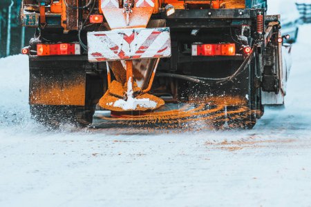 Téléchargez les photos : Un camion de chasse-neige applique du sel et du sable pendant que le camion travaille au nettoyage de la route enneigée. Entretien des routes et des infrastructures pendant l'hiver. Rouille et dommages au train d'atterrissage du véhicule. - en image libre de droit