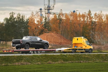 Tow truck with a broken pick-up truck on the interstate highway. Tow truck transporting modern crew cab truck on a road. Roadside Rescue. Car service transportation concept.