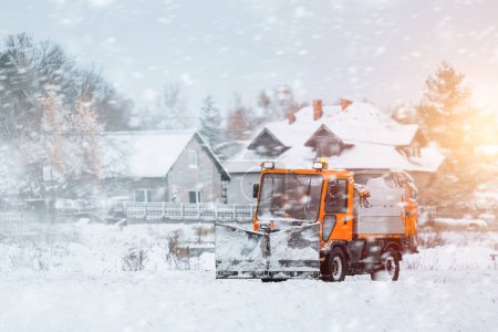 Un camión naranja con un esparcidor de sal y arena limpia la nieve y el hielo de la carretera. El vehículo de servicio de invierno funciona para hacer que las carreteras públicas sean seguras y evitar la corrosión.