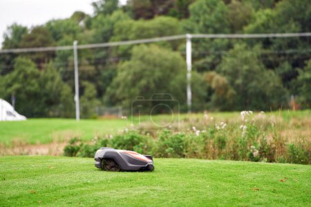 Téléchargez les photos : Robotique tondeuse à gazon sur herbe, vue latérale. Gros plan isolé de la tondeuse automatique. Entretien intelligent des pelouses. Taille-herbe électronique. - en image libre de droit