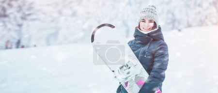 Snowboarding on a winter day. A young woman with her snowboard on a white slope. She is having fun and feeling the adrenaline. Stunning background view of the snow-covered pines. Girl in winter