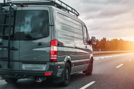 Concept of traveling with a van and enjoying the outdoor adventures. The ultimate van camping in Europe. Offroad modern van for traveling with a ladder on the back and an additional baggage roof rack.