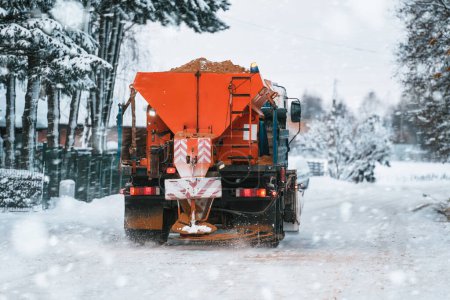 Téléchargez les photos : Un camion de chasse-neige applique du sel et du sable pendant que le camion travaille au nettoyage de la route enneigée. Entretien des routes et des infrastructures pendant l'hiver. Rouille et dommages au train d'atterrissage du véhicule. - en image libre de droit