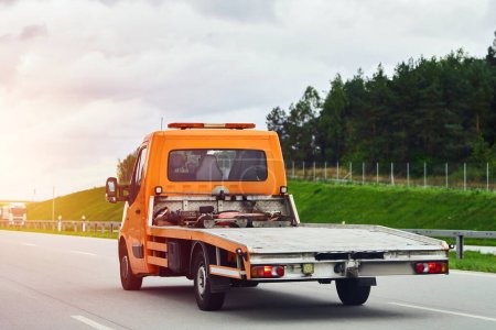 Photo for A rollback tow truck transports a broken car on the public road. Car failure during the journey. Roadside assistance in action. - Royalty Free Image