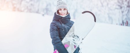 Snowboard in der alpinen Natur. Eine junge, hübsche Frau mit einem Brett macht einen Sprung auf einen verschneiten Hügel. Sie hat Spaß und spürt den Nervenkitzel.