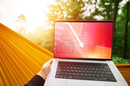Photo for A Bad Day for a Freelancer in the Park. Crypto Trading with a Laptop and a Red Arrow on the Chart - Royalty Free Image