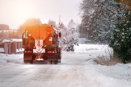 Téléchargez les photos : Un camion de chasse-neige applique du sel et du sable pendant que le camion travaille au nettoyage de la route enneigée. Comment le sel et le sable endommagent les parties métalliques d'un camion labourant la neige sur une route d'hiver - en image libre de droit