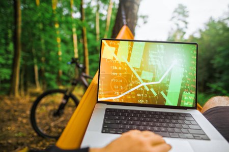 Photo for A Freelancer Trading Crypto in the Park with modern Laptop and Enjoying the Green Market Growth. Lifestyle of Smart Working in Nature with Crypto Trading and an Apple Laptop - Royalty Free Image