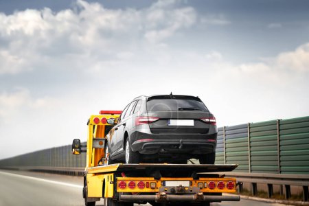 Photo for A car crash on the highway leads to the arrival of a tow truck. The transporter picks up the wrecked car and carries it away. The sky is cloudy and the traffic is slow - Royalty Free Image