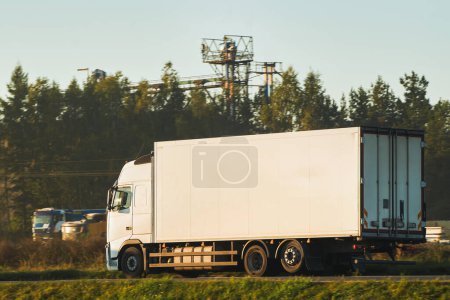 Modern white trucks with semi-trailers drive on a highway. Transporting cargo containers for commercial and industrial purposes. Sustainable logistics and efficient delivery methods to ship goods.