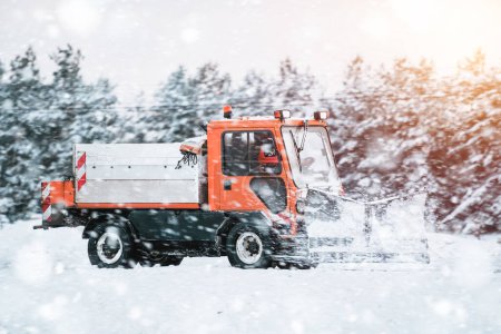 Téléchargez les photos : Entretien routier en hiver. un tracteur équipé d'un épandeur pulvérise un mélange de sel et de sable sur la route glacée et enneigée. Le véhicule appartient au service municipal qui fait fondre la neige - en image libre de droit