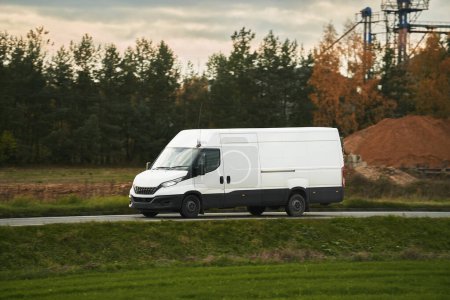 Téléchargez les photos : Une maquette d'un van blanc avec une pellicule vide à personnaliser. Un véhicule utilitaire pour votre service de livraison et de transport. Petit camion blanc isolé sur la route. - en image libre de droit