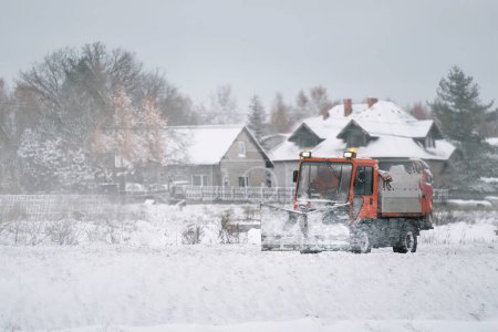Téléchargez les photos : Entretien routier en hiver. un tracteur équipé d'un épandeur pulvérise un mélange de sel et de sable sur la route glacée et enneigée. Le véhicule appartient au service municipal qui fait fondre la neige - en image libre de droit