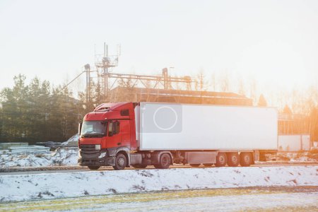 Téléchargez les photos : Un grand camion de transport transporte des marchandises commerciales sur une route enneigée. La semi-remorque fait face à une tempête de neige dangereuse et des conditions routières glissantes. - en image libre de droit