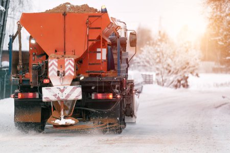 Foto de Un camión de quitanieves aplica sal y arena mientras el camión trabaja para limpiar el camino cubierto de nieve. Mantenimiento de carreteras e infraestructuras durante el invierno. Oxido y daños en el tren de rodaje del vehículo. - Imagen libre de derechos