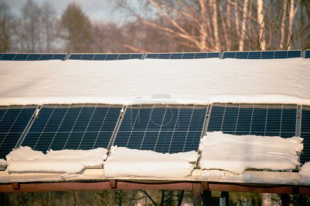 Foto de La nieve se derrite a partir de paneles solares fotovoltaicos cubiertos instalados en el techo de la casa para producir energía eléctrica sostenible. Concepto de baja eficacia de la electricidad renovable en los climas de la región norte - Imagen libre de derechos