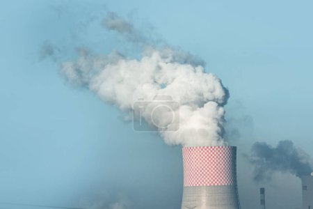 La fumée et la vapeur s'élèvent d'une centrale électrique dans un champ vert sous un ciel bleu