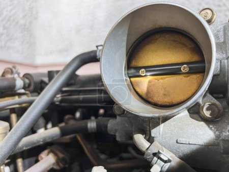 "The effects of carbon on a throttle valve of a car engine". La lame de la vanne est recouverte de saleté et de carbone, ce qui nuit aux performances et à l'efficacité du moteur.