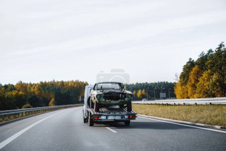 Photo for A car crash on the highway leads to the arrival of a tow truck. The transporter picks up the wrecked car and carries it away. The sky is cloudy and the traffic is slow - Royalty Free Image