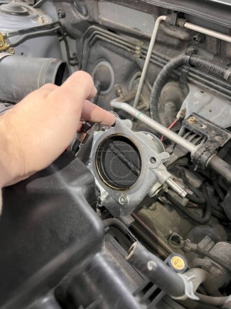 The repair and maintenance of an electronic throttle body in a car engine. The photo depicts the intake valve, the metal body, and the electronic control of the throttle body.