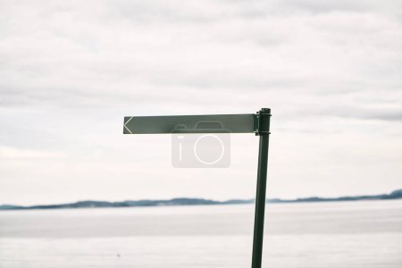 Poteau de signalisation métallique blanc contre un paysage marin serein, idéal pour le placement de texte. Panneau directionnel vide avec fond marin