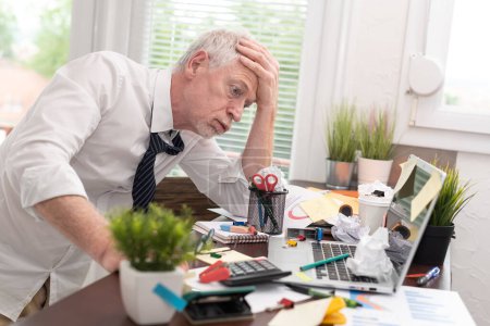 Photo for Overworked senior businessman sitting at a messy desk - Royalty Free Image
