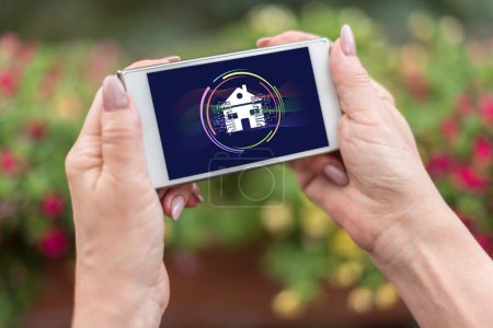 Téléchargez les photos : Mains féminines tenant un smartphone avec concept de maison intelligente - en image libre de droit