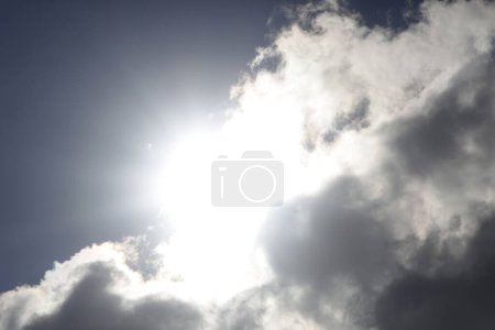 Photo for The bright sun shines from behind dark clouds against a blue sky. - Royalty Free Image