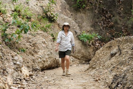 Geóloga mujer sosteniendo lupa y portátil trabajando examinando roca, suelo, arena en la naturaleza. Los arqueólogos exploran el campo. Investigación medioambiental y ecología.