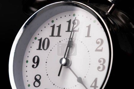 Foto de Primer plano de un reloj despertador retro sobre un fondo negro. Reloj manos se mueven rápido, el comienzo de la hora 12: 00 AM o 12: 00 PM. - Imagen libre de derechos