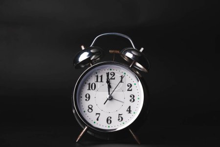 Foto de Primer plano de un reloj despertador retro sobre un fondo negro. Reloj manos se mueven rápido, el comienzo de la hora 12: 00 AM o 12: 00 PM. - Imagen libre de derechos