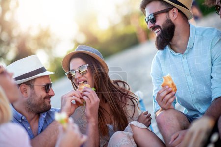 Téléchargez les photos : Groupe de personnes mangeant des sandwichs pendant le pique-nique sur la plage. - en image libre de droit