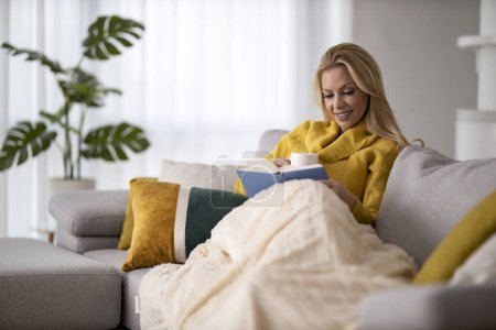 Téléchargez les photos : Woman relaxing at home with cup of tea and book. Education concept. - en image libre de droit