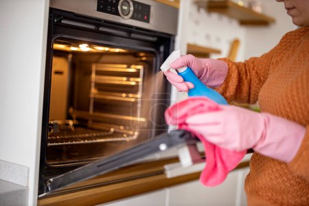 Téléchargez les photos : Young woman cleaning oven with rag in kitchen.Woman cleaning oven in kitchen. - en image libre de droit
