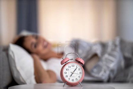 Foto de Woman sleeping near bed side ,alarm clock is in front of her.Morning routine and wake up from bed. - Imagen libre de derechos