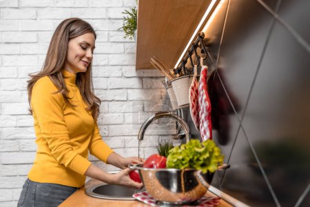 Téléchargez les photos : Woman washing vegetables in kitchen at home.Hygiene, health care and food concept. - en image libre de droit