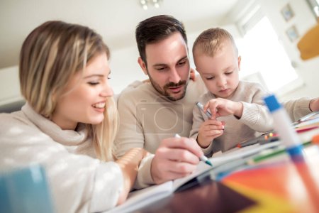 Téléchargez les photos : Mère et père dessinent ensemble avec leur enfant à la maison. - en image libre de droit