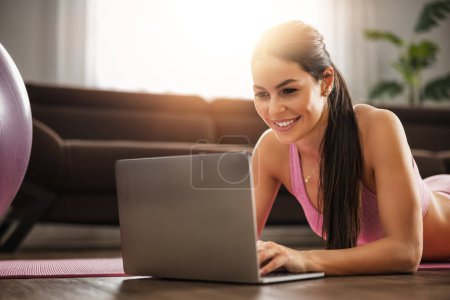 Téléchargez les photos : Femme de fitness en vêtements de sport faisant de l'exercice à la maison devant un ordinateur portable, regardant la vidéo de fitness.. - en image libre de droit
