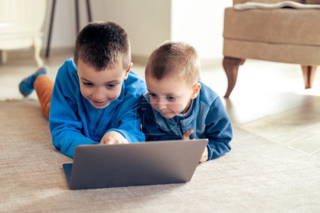 Foto de Niños viendo dibujos animados en el ordenador portátil en casa en la sala de estar. - Imagen libre de derechos
