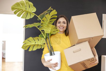 Téléchargez les photos : Femme emménageant dans un nouvel appartement, tenant des boîtes en carton et une usine. - en image libre de droit