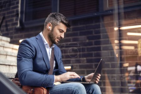 Téléchargez les photos : Homme d'affaires travaillant sur un ordinateur portable. Homme assis dans les escaliers à l'extérieur et travaillant sur ordinateur portable, vérifier email. - en image libre de droit