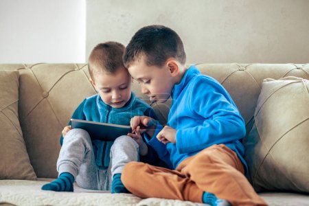 Téléchargez les photos : Garçons jouant à des jeux vidéo sur la tablette à la maison. - en image libre de droit