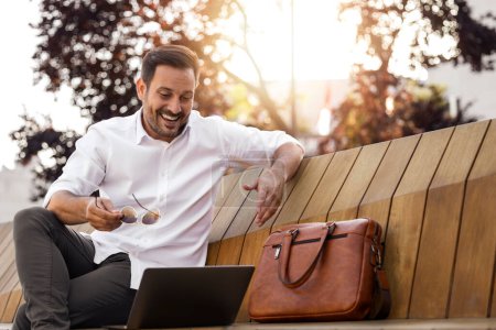 Téléchargez les photos : Jeune homme d'affaires est assis au parc et en utilisant un ordinateur portable
. - en image libre de droit