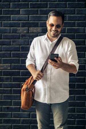 Foto de Hombre de negocios guapo usando el teléfono inteligente en la ciudad.Retrato de un joven hombre de negocios al aire libre. - Imagen libre de derechos