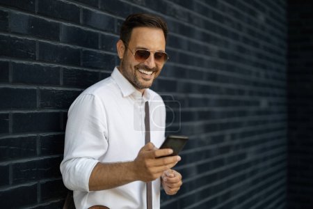 Foto de Hombre de negocios guapo usando el teléfono inteligente en la ciudad.Retrato de un joven hombre de negocios al aire libre. - Imagen libre de derechos