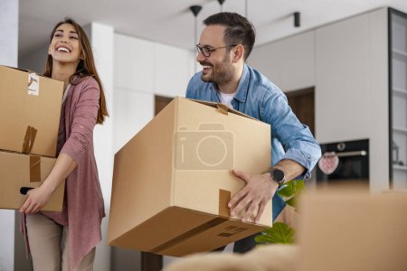 Photo for Cheerful married couple speaking in good mood discussing decor of new home while standing and holding cardboxes. Happy moving day. - Royalty Free Image